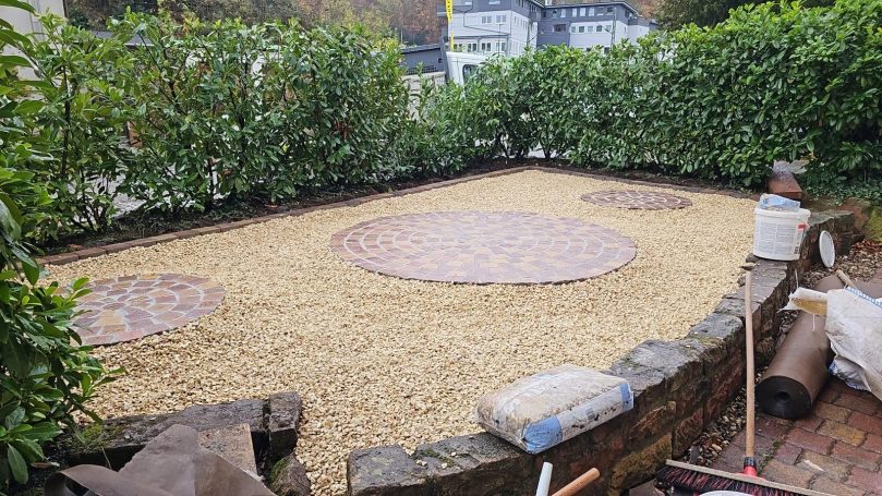 Gartenbereich mit Kies und runden Pflastersteinen, umgeben von Hecken.